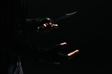 Obraz na płótnie Canvas Cropped view of african american bandit in gloves holding knife isolated on black