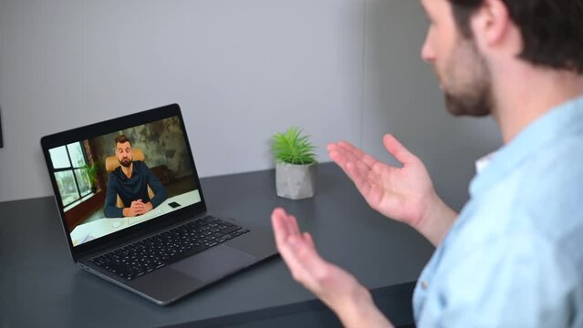 E-learning. Young man using laptop computer for watching online courses, webinars, male tutor on the screen. Two male coworkers talking via video connection