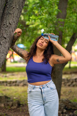 A beautiful girl with tattoos puts a bottle of water to her head in the park. The girl got...