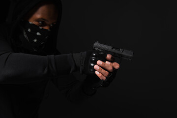 African american bandit with obscure face holding handgun isolated on black - obrazy, fototapety, plakaty