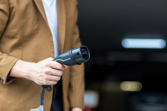 Man Hand Holding Electric Car Charger. Electric Vehicle EV Charging Station And Charger. Human Hand Is Holding 