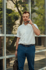 A young businessman man is talking on a mobile phone near the glass facade