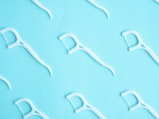 Pattern of white dental floss with a plastic toothpick on blue. Dental concept