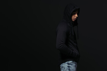 Naklejka na ściany i meble Side view of african american hooligan in hoodie standing isolated on black