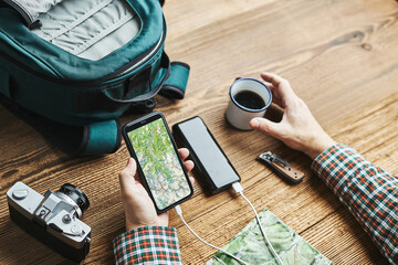 Man planning next vacation trip while journey searching travel destination and routes using navigation map on mobile phone. Charging smartphone with power bank. Using technology while travelling