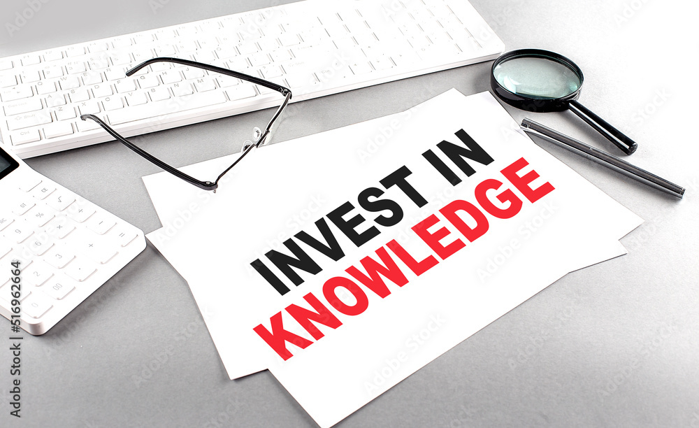 Poster invest in knowledge text on a paper on a gray background near a calculator and a white keyboard