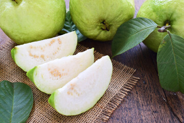 Three slices of green guava fruit with leaf on sackcloth and wooden table.