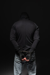 Naklejka na ściany i meble Back view of african american bandit in hoodie and handcuffs standing isolated on black