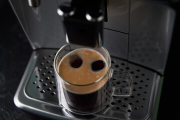 Freshly brewed coffee is poured from the coffee machine into glass cups.