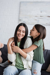 brunette girl with closed eyes kissing happy babysitter in living room.