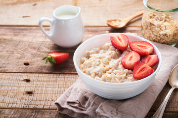 Oatmeal. Bowl of oatmeal porridge with strawberry, almond and milk on old wooden dark table background. Top view in flat lay style. Natural ingredients. Hot and healthy breakfast and diet food.