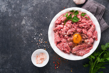 Raw minced meat. Ground meat beef, pork or lamb spices, herbs and eggs on white plate on black old concrete background. Fresh minced meat ready for cooking. Food cooking background. Top view.