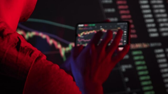 Trader analyze cryptocurrency charts on a smartphone screen in the dark. Man looking at currency charts in the stock market. Trading stocks, bitcoins, futures, btc, investment market. Finance concept.