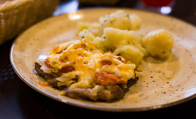 meat baked with cheese with boiled potatoes served on a plate in restaurant