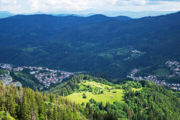 Fototapeta na wymiar Mountain valley sheltered by vegetation and spruce forests with village of Smolyan with meadows where sheep graze
