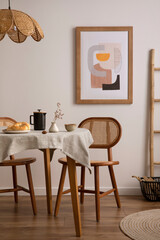 The stylish dining room with round table, rattan chair, lamp, poster and kitchen accessories. Beige wall with mock up poster. Home decor. Template.