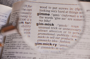 The definition of the word Gimmick in a dictionary, under magnifying glass, translator and language...
