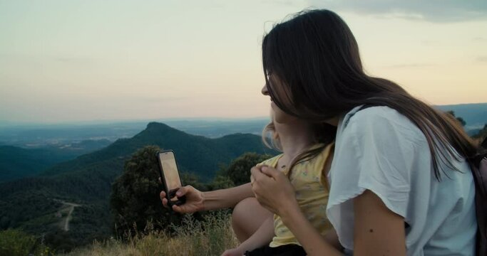 Family on mountain travel at summertime vacation. Happy young adult woman with daughter making selfie photo using mobile phone. Mother take a picture on smartphone with toddler girl. Handheld footage