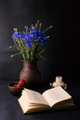 Still life with strawberries and cornflowers on a black background