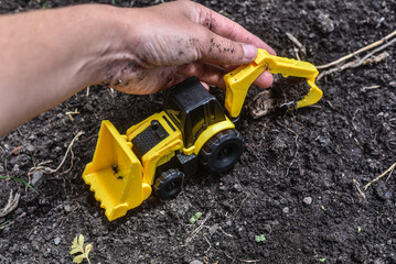 Toy digger with child's hand digging in muddy soil