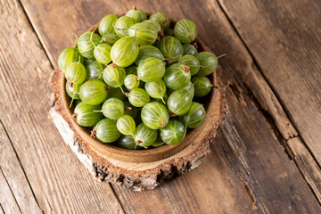 Green gooseberries in a wooden bowl. Harvest berries on a wooden table. Gooseberry summer vitamin food.