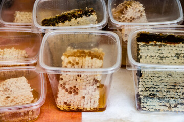 Wax honeycombs with honey in plastic containers. Sale of homemade honey at the fair. Honeycomb texture close up.