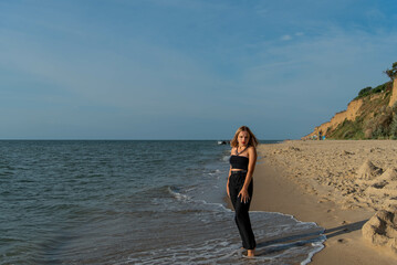 Woman wearing black dress walking on beach. See view