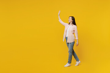 Fototapeta na wymiar Full body side view young happy smiling woman she 30s wear striped shirt white t-shirt walking going strolling waving hand isolated on plain yellow background studio portrait People lifestyle concept