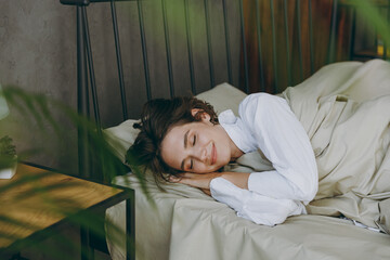 Young calm woman wear white shirt pajama she lying in bed hands folded under head rest relax spend...