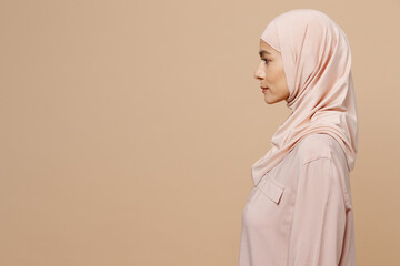 Side view young arabian asian muslim woman 30s she wearing abaya hijab pink clothes isolated on plain pastel light beige background studio portrait. People uae middle eastern islam religious concept.