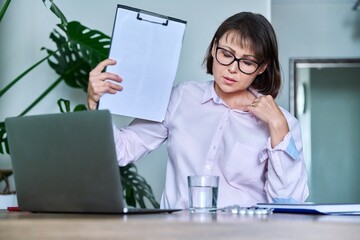 Middle-aged woman suffering from heat, overheated, cooled by fan and fan