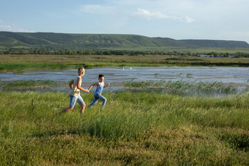 Fototapeta na wymiar Two brothers in jeans and t-shirts run along the pond competing in speed. Summer sunny day near the pond. Summer holidays in the countryside