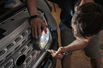 The mechanic is in the process of installing and adjusting the headlights on the car. The process of installing LED optics on a car, selective focus. Repair and restoration of the headlight.