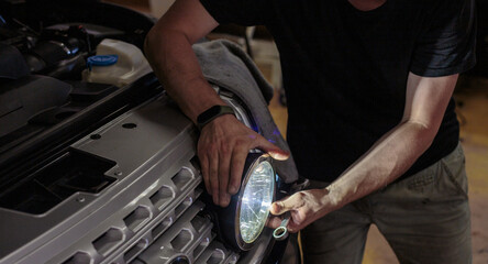 The mechanic is in the process of installing and adjusting the headlights on the car. The process...