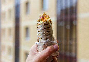 A man holds a shawarma. Street food. Food on the go. The concept of street food. Shawarma in lavash...