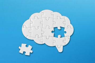 Brain shaped white jigsaw puzzle on blue background, a missing piece of the brain puzzle, mental health and problems with memory