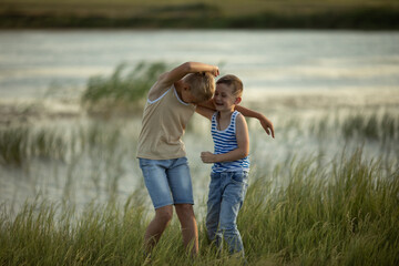 Two brothers in jeans and t-shirts have fun and laugh near the pond. Summer sunny day near the pond. Summer holidays in the countryside. Happy childhood