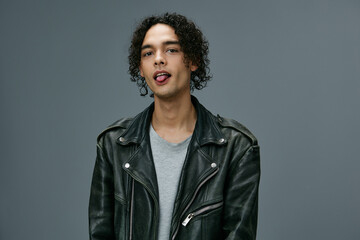 Obraz premium Cute attractive stylish tanned curly man leather jacket posing isolated on over gray studio background. Cool fashion offer. Huge Seasonal Sale New Collection concept. Copy space for ad