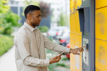  A black man with a smartphone in his hands near the self-service mail terminal. Parcel delivery...