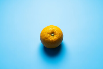 Top view of whole orange with shadow on blue background.