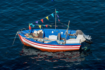 Boat with colorful flags in the blue sea in Camara dos Lobos, Madeira Island, Portugal