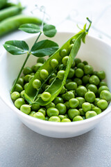 Green fresh peas, snack pea in a white bowl on a neutral grey background. Top view. Summer garden vegetables.