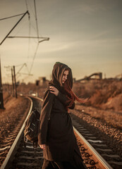 Young lonely woman walking along railway track, on background of industrial city, despair and depression portrait,  in dramatic and anti-utopia style