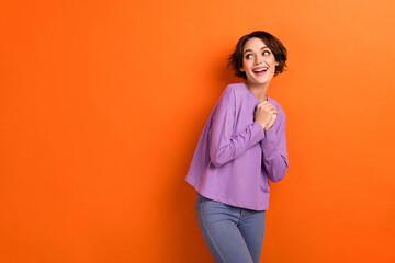 Photo of dreamy adorable girl dressed purple pullover looking empty space isolated orange color background