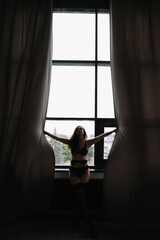 Gorgeous woman wearing black lingerie indoors. Portrait of a beautiful dreamy girl in a black underwear by the window