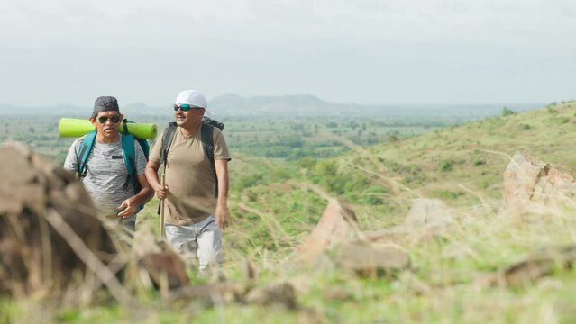 Back view shot of middle aged hikers with backpack climbing on top of hill - concept of trekking, freedom and outdoor leisure activities
