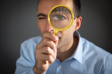 Caucasian man holding magnifying glass and looking at camera.