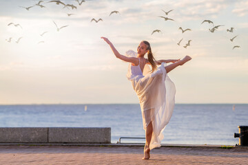 A dancing ballerina in a white flying skirt and tights on the ocean embankment or on the sea beach,...