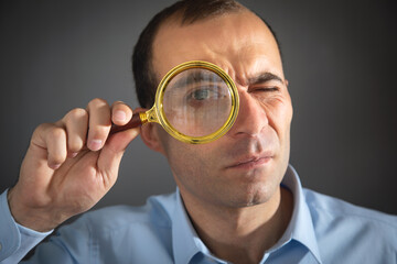 Caucasian man holding magnifying glass and looking at camera.