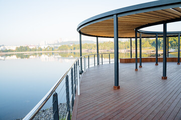 Wooden pier of round shape on the river bank, park for walking on the pond, country house with a view of the lake, art object in the city, a place for people to relax, relaxation and silence